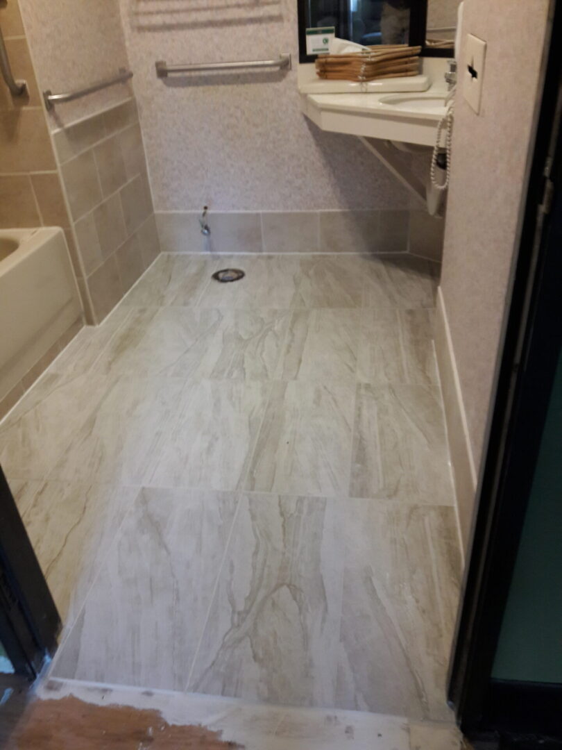 A bathroom with white tile and wood floors.