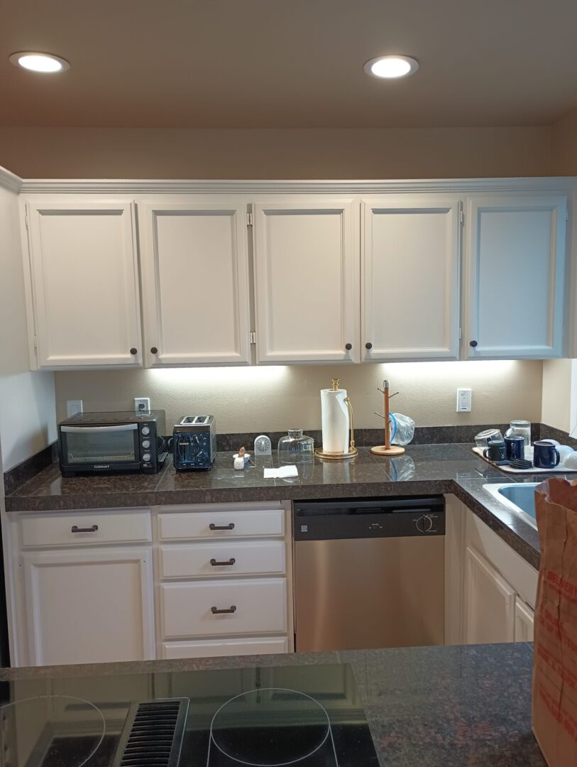 A kitchen with white cabinets and black counter tops.